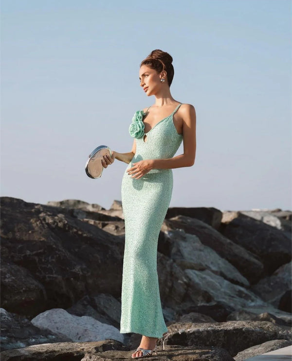Woman in a light green dress standing on rocks with a clear sky background