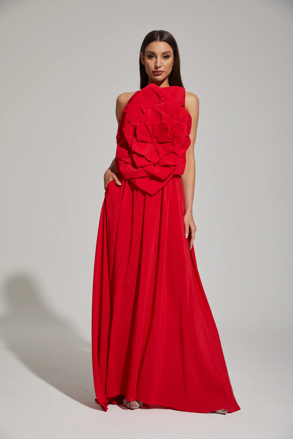 Woman wearing a red evening gown with floral details on a white background