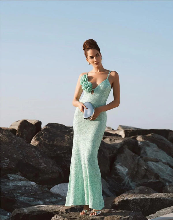 Woman in a light green evening gown standing on rocks with a clear sky background