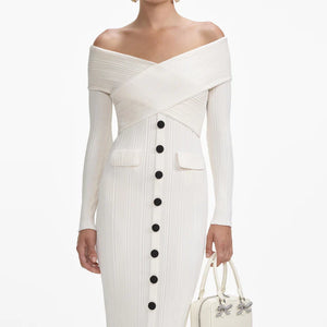White off-shoulder dress with black buttons and a handbag on a white background