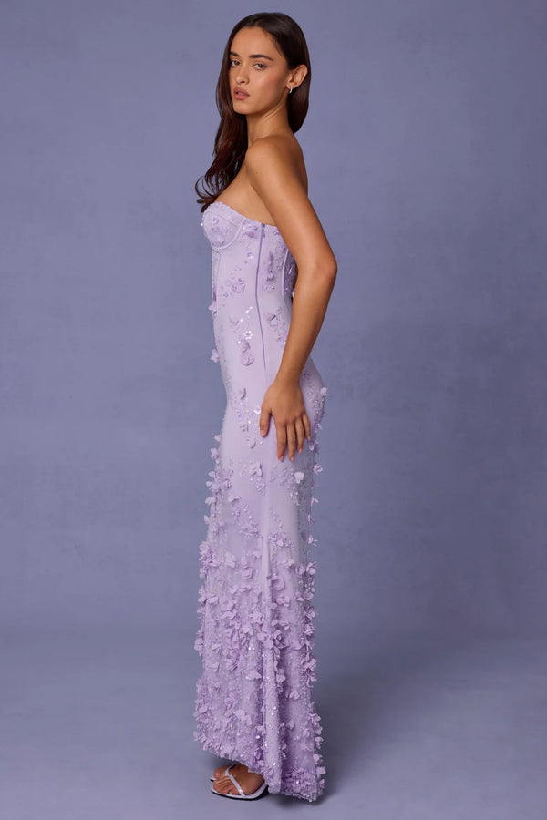 Woman wearing a strapless, floral embroidered purple gown against a plain background