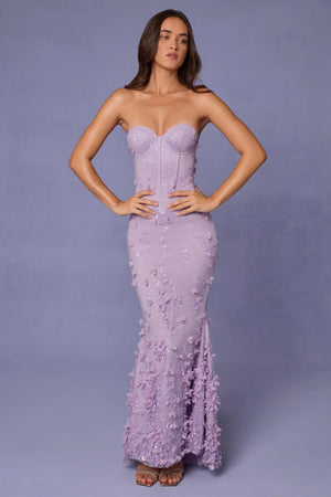 Woman wearing a strapless, embroidered lilac gown against a plain background