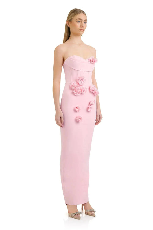 Woman wearing a pink strapless gown with floral embellishments on a white background