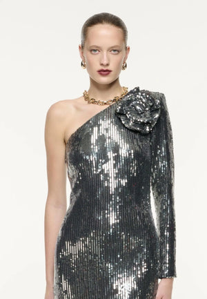 Woman wearing a silver sequin one-shoulder dress with a floral detail on a white background